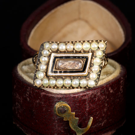 Georgian mourning ring with rectangular bezel displaying woven hairwork under crystal, bordered by black and white enamel and two rows of seed pearls, circa 1810