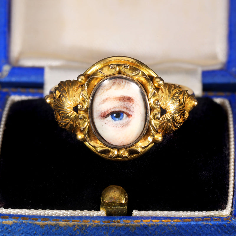 Georgian lover's eye ring in gold with a hand-painted watercolour miniature of a blue eye on ivory, set within an ornate scrollwork frame