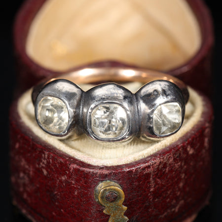 Georgian three-stone paste ring with clear hand-cut paste stones set in silver collets on a gold band, imitating diamonds, displayed in a red leather ring box