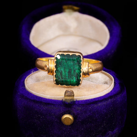 Antique 19th century step cut emerald in a gold ring with crimped bezel setting, showing deep green colour characteristic of chromium trace elements in beryl
