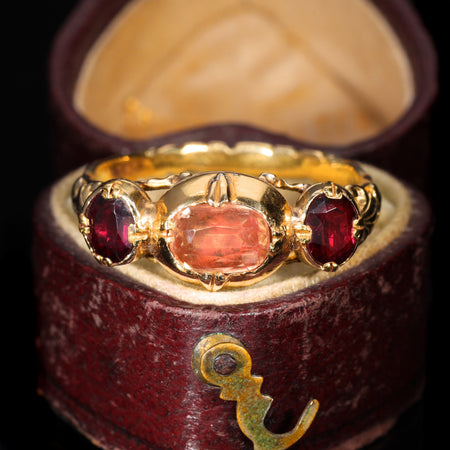 Antique French 19th-century ring in gold with a central topaz flanked by two garnets, displaying ornate scrollwork shoulders typical of continental European jewellery